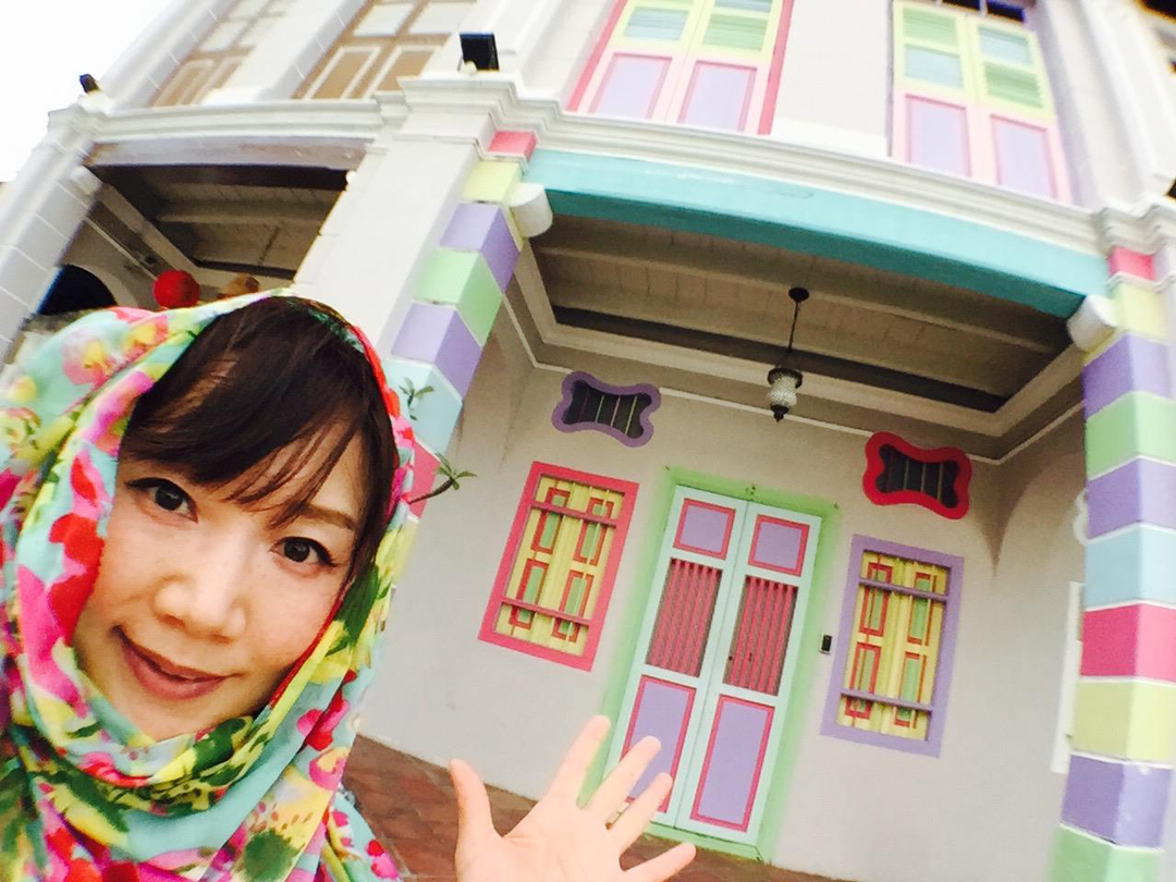 パステルカラーの可愛い家の前で、ストールをヒジャブ風に