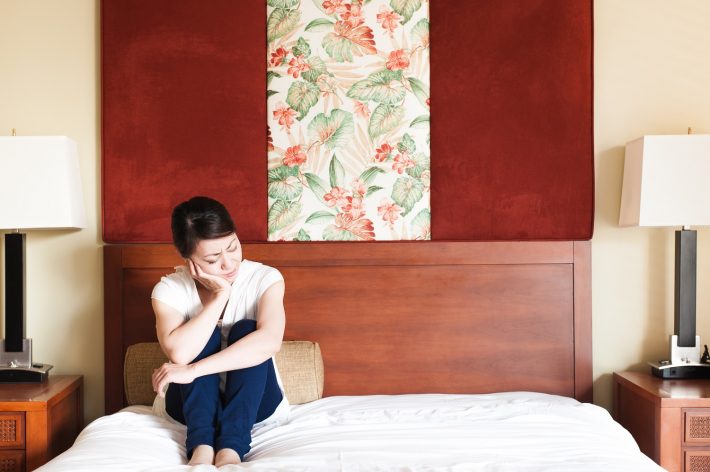 ベッドの上に座って悩んでいる女性