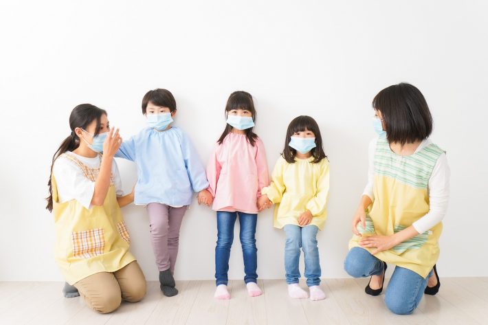 マスクを付けて幼稚園で遊ぶ子どもたちの先生