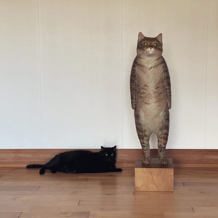 猫の彫刻のとなりでまったりする黒猫のひなた