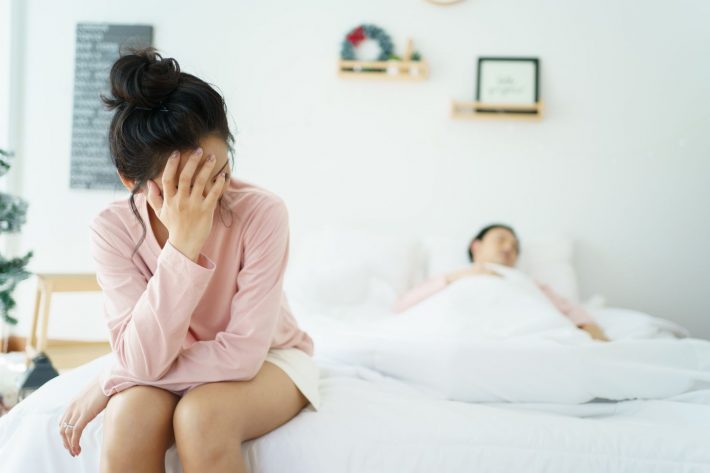 ベッドの上で悩む女性