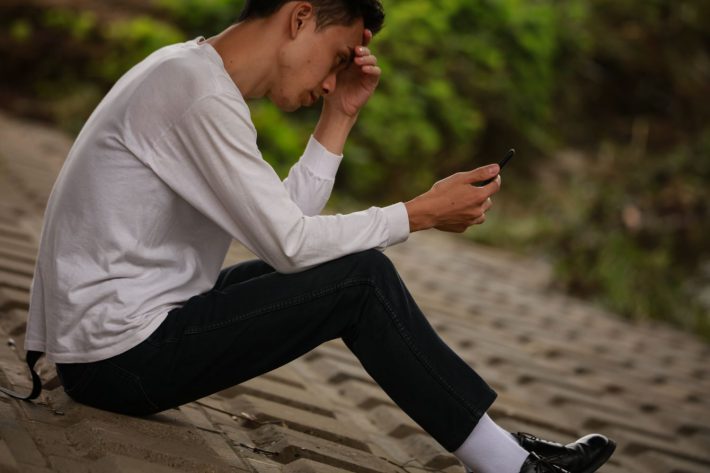 スマートフォンを見て頭を抱える男性