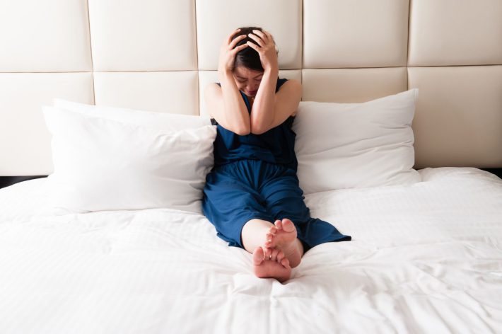 ベッドの上で頭を抱える女性