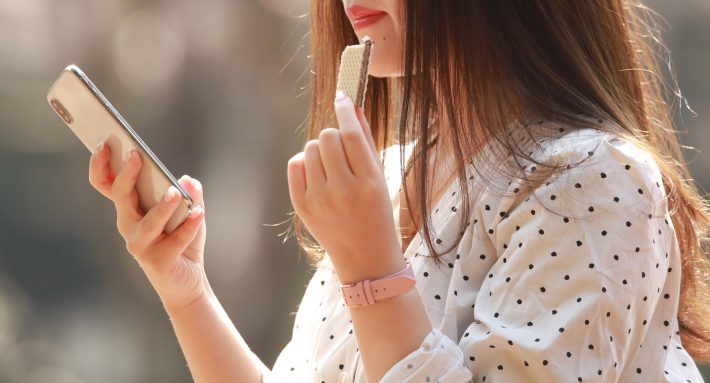 ウェハースを食べながらスマホを見る女性