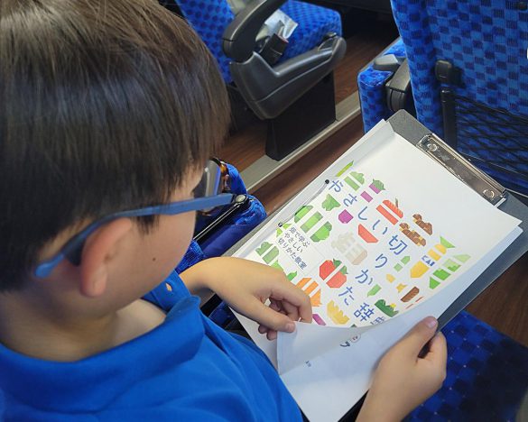 農場に到着する前に、バスの中で包丁使いについて説明を聞く様子