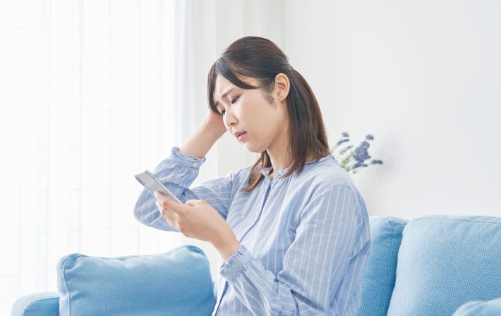 リビングで頭を抱えてスマホを使う女性