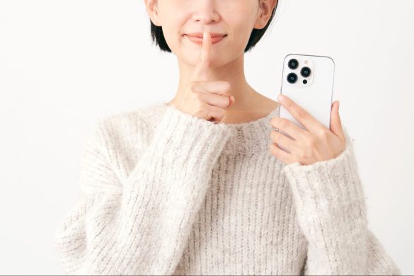 スマホを持って内緒のジェスチャーをする中年女性