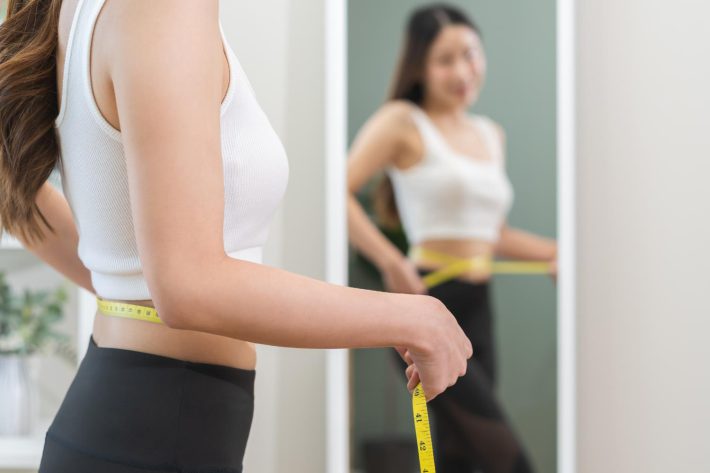 鏡の前でウエストをはかる女性