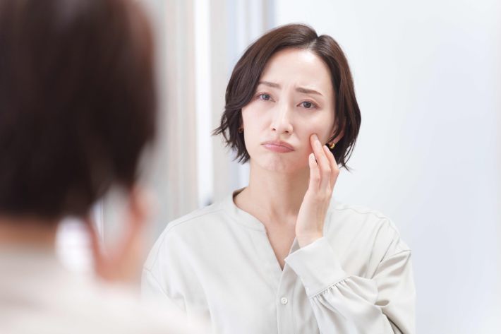 鏡を見てメイクに悩むミドル女性