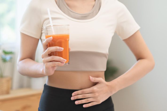野菜ジュースを飲みながらお腹に手をあてる女性