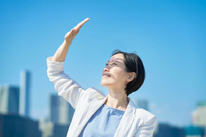 強い日差しを手でさえぎる女性